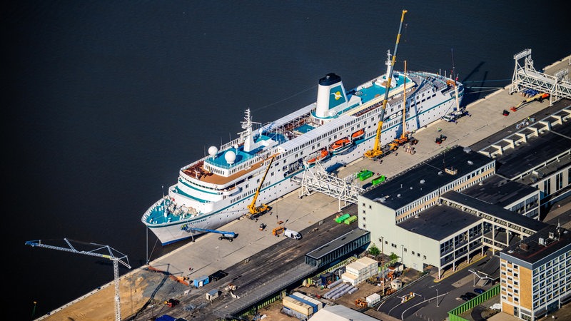 Blick aus der Luft auf ein Kreuzfahrtschiff, das an einer Kaje liegt.