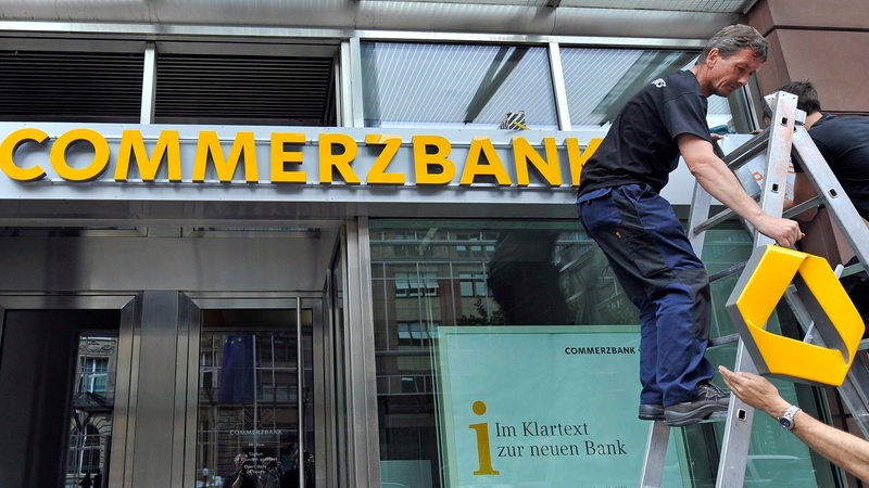 Ein Bauarbeiter befestigt das Commerzbanklogo an einer Filiale