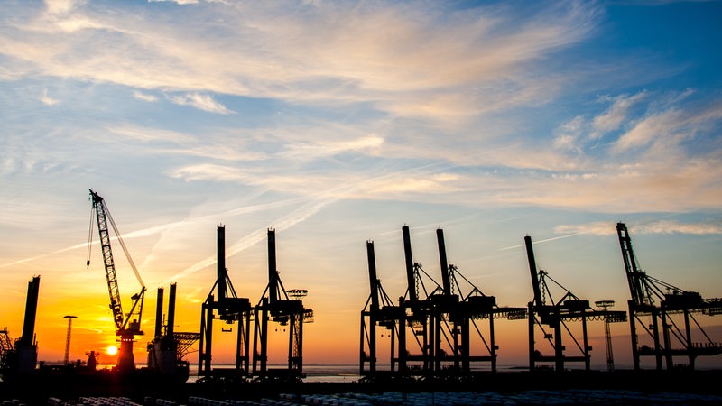 Die Sonne geht hinter Ladebrücken am Containerterminal in Bremerhaven unter.