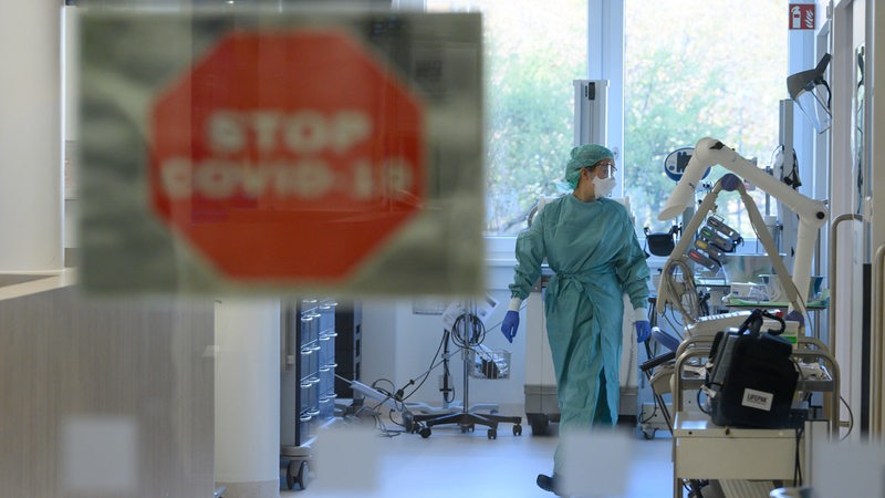 Eine Intensivpflegerin läuft in der Corona-Intensivstation eines Krankenhauses über den Gang während im Vordergrund ein Schild mit der Aufschrift «Stop Covid-19» an der Tür zu sehen ist.