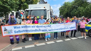 Mitglieder des Senats halten beim CSD ein Plakat hoch.