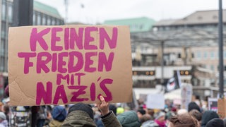 Ein Mensch hält ein Schild in die Höhe, auf dem steht: "Keinen Frieden mit Nazis"