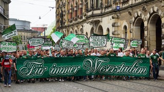 Hunderte junge Menschen laufen mit Schildern und einem großen grün-weißen Transparent mit der Aufschrift Für immer Weserstadion durch die Bremer Innenstadt. 