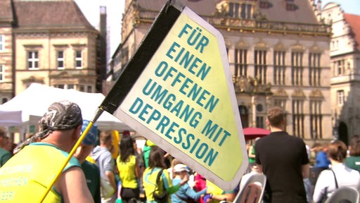In der Bremer Innenstadt ist der Bundesauftakt der "MUT-TOUR" zu sehen. Auf einem Schild steht "Für einen offenen Umgang mit Depression".