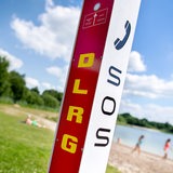 Eine Notrufsäule der DLRG, im Hintergrund eine Badestrand.