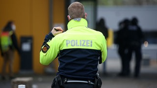 Rückenansicht eines Polizisten mit Warnweste vor einer Schule