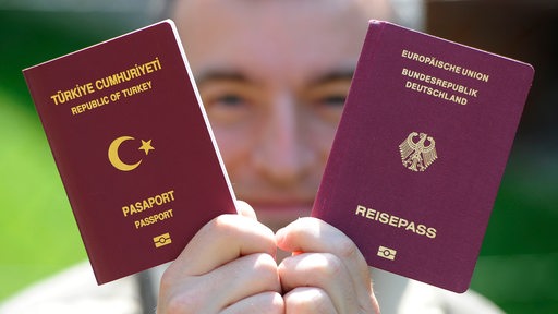 Ein türkischer und eine deutscher Reisepass werden von einem Mann in die Kamera gehalten.
