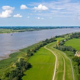 Eine Luftaufnahme zeigt einen Fluss zwischen grünen Wiesen.