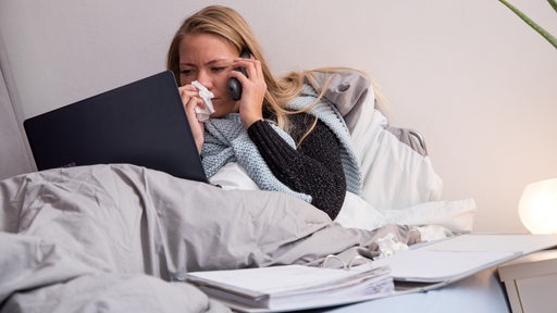 Eine Frau liegt krank im Bett und telefoniert.