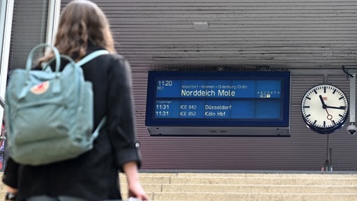 Eine Frau geht mit einem Koffer eine Treppe zum Bahnsteig hoch