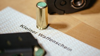 Ein Kleiner Waffenschein liegt zwischen einer Schreckschuss-Pistole "Walther P22", einem Magazin und einer Knallpatrone.