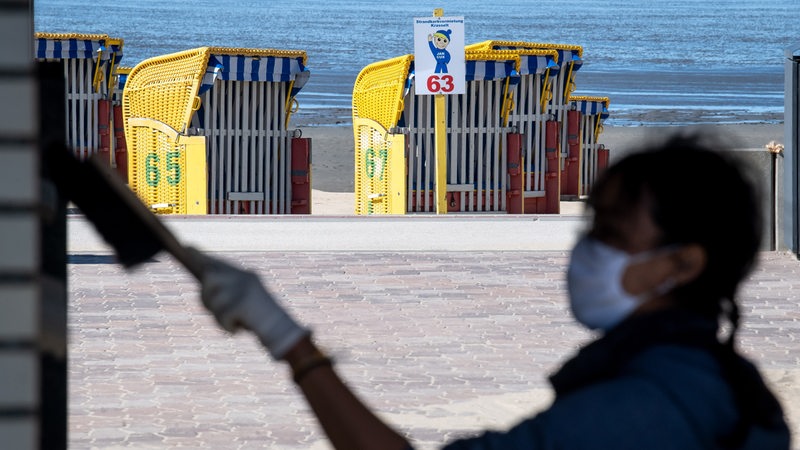 A woman with a protective mask brushes the facade of a building in front of the beach in Cuxhaven. 