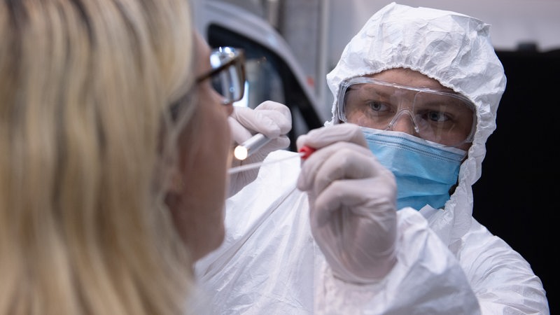 A person in a protective suit takes a throat swab from a woman.