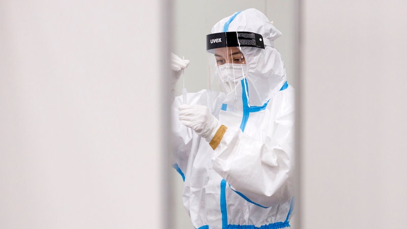 A woman packs a smear in a swab tube.  She wears protective clothing.