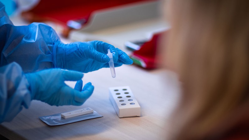 Hands in blue gloves hold a glass tube