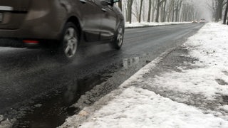 Ein Auto fährt durch Schneematsch über eine Landstraße