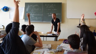 Eine Schulklasse im Unterricht, vorne steht ein junger Lehrer (Symbolfoto)