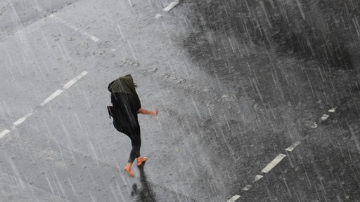 Eine Frau geht bei Regen mit einem Regenschirm über die Straße.