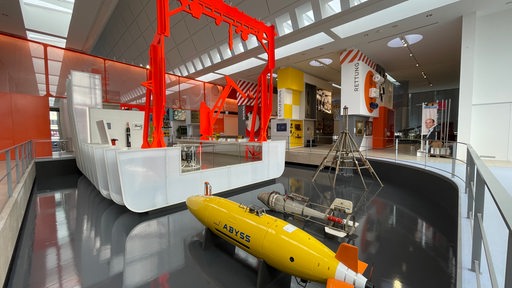 Kleine U-Boote sind hinter einem Schiffsmodell ausgestellt.
