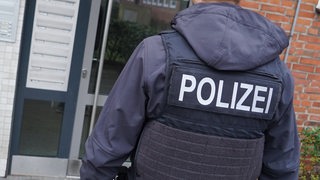 Ein Polizist steht vor einem Haus, in dem eine Wohnung durchsucht werden soll.