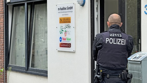 Ein Polizeibeamter steht vor der Tür der m-haditec Gmbh während einer Durchsuchung der Geschäftsräume in Bremen-Huchting.