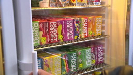 In einem Kühlschrank sind mehrere bunte Päckchen einer Softdrinkmarke zu sehen.
