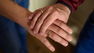 Zwei Menschen mit Eheringen an den Fingern halten Hände