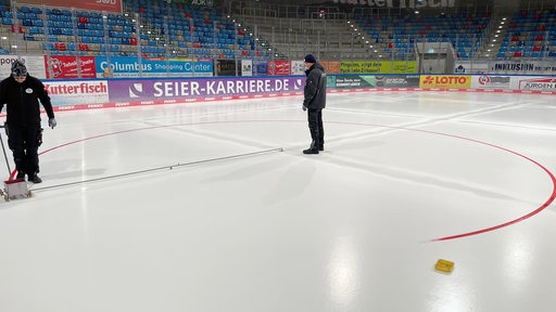 Ein Arbeiter zieht mit einem kleinen Farbwagen an der Hand den roten Kreis auf die Eisfläche in der Eisarena Bremerhaven.