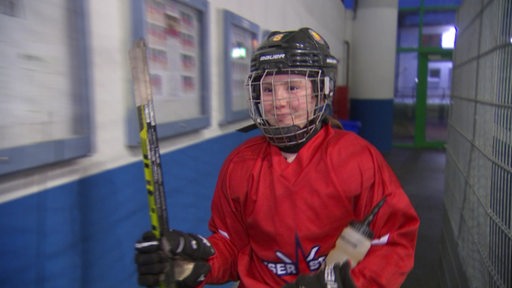 Nachwuchs-Eishockeyspielerin Annica Busch mit Helm auf dem Kopf und in voller Ausrüstung auf dem Weg zur Eisfläche.