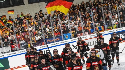 Die deutsche Eishockey-Nationalmannschaft der Frauen läuft nach dem Deutschland Cup vor dem Fanblock und den schwarz-rot-goldenen Fahnen vorbei.