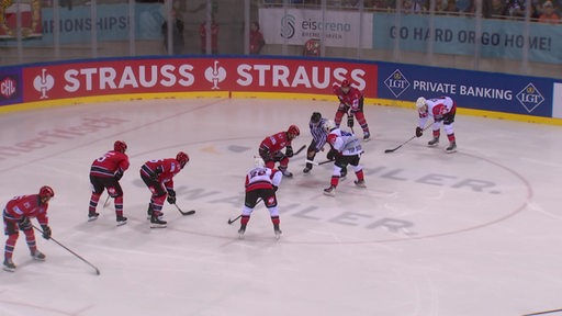 Eishockeyspieler zweier Teams stehen während eines Bullys auf einem Spielfeld