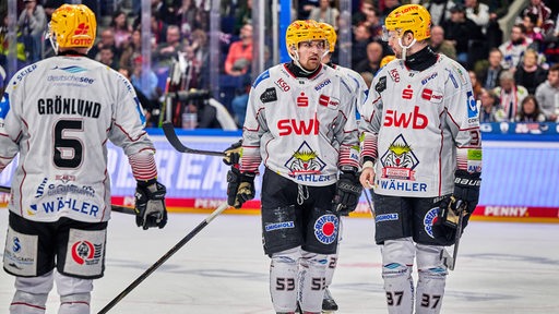 Einige Eishockey-Spieler der Fischtown Pinguins aus Bremerhaven stehen etwas ratlos während eines Spiels beisammen.