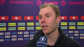 Eishockey-Torwart Maximilian Franzreb von den Fischtown Pinguins steht nach einem Champions-League-Spiel vor einer Werbewand beim Interview.