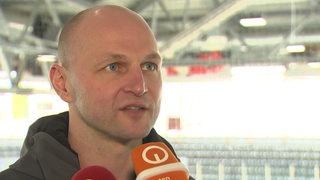 Sebastian Furchner, Eishockey-Manager der Fischtown Pinguins, steht in einer Eishalle in Bremen beim Interview.