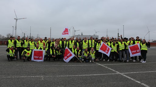 Menschen mit Warnwesten und Fahnen posieren auf einem Parkplatz für ein Gruppenfoto.