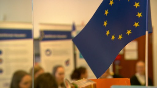 Im Vordergrund ist die europäische Flagge zu sehen und im Hintergrund erkennt man mehrere Jugendliche.