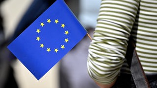 Der Arm einer Person, die eine EU-Flagge hält, ist zu sehen. 