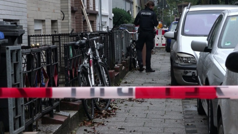 Ein Polizist steht hinter einem Flatterband auf einer Straße.