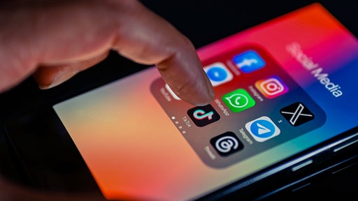 Ein Finger tippt auf einem Handy-Display mit Apps aus Social Media.