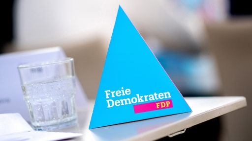 Ein Wasserglas steht auf einem Tisch, daneben ein dreieckiger Aufsteller mit der Aufschrift "Freie Demokraten – FDP".