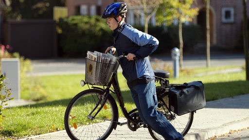 Ein Jugendlicher auf einem Fahrrad mit Zeitungen im Fahrradkorb versucht einen Bordstein hochzufahren.