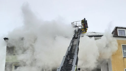 Ein Leiterwagen der Feuerwehr steht vor einem Haus, aus dem Qualm kommt.