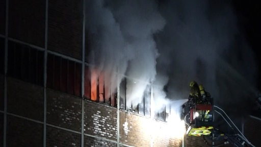 Feuerwehrleute löschen von einer Leiter aus einen Brand in einem Fenster