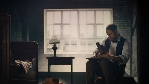 In einer Szene des Film "Bernhard Hoetger - Zwischen den Welten" sitzt ein Mann auf einem Stuhl in einem Zimmer.