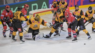 Drei Eishockeyspieler der Fischtown Pinguins in roten Trikots sind von Spielern in gelben Trikots umringt.