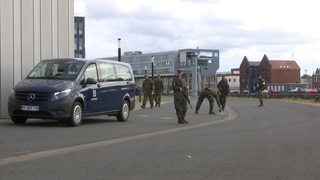 Mehrere Soldaten stehen neben einem Kleinbus auf einer Straße.