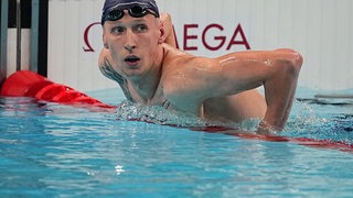 Ein Mann mit Schwimmhaube und Schwimmbrille beugt sich im Wasser über eine Barriere