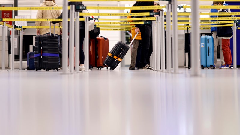 Fluggäste stehen mit ihren Koffern in einer Schlange am Flughafen.