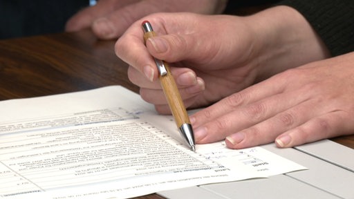 Eine Person füllt mit einem Kugelschreiber ein Formular oder einen Antrag aus.