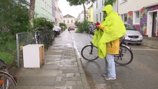 Eine Frau macht ein Foto von Sperrmüll am Wegesrand.